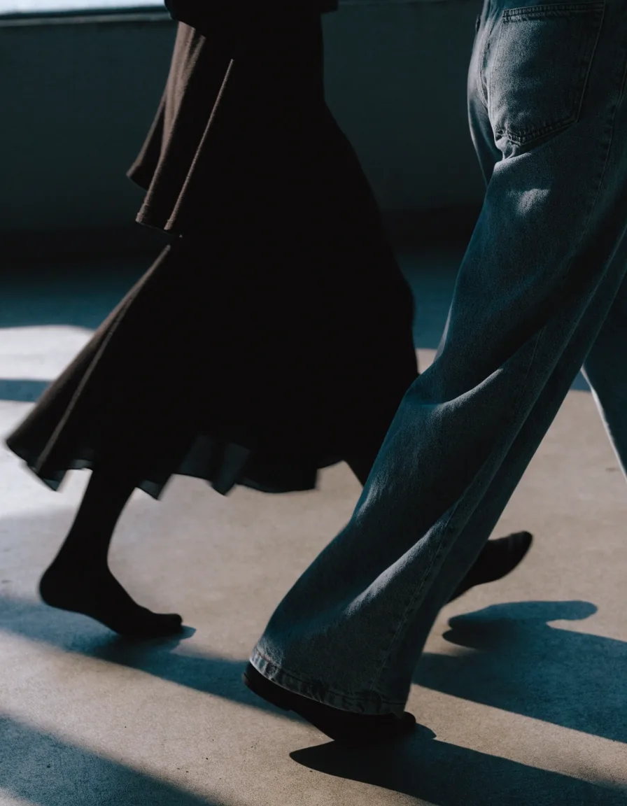 Two figures mid-stride on a bare concrete floor, cropped at the shoulders, hems blurred by the walk